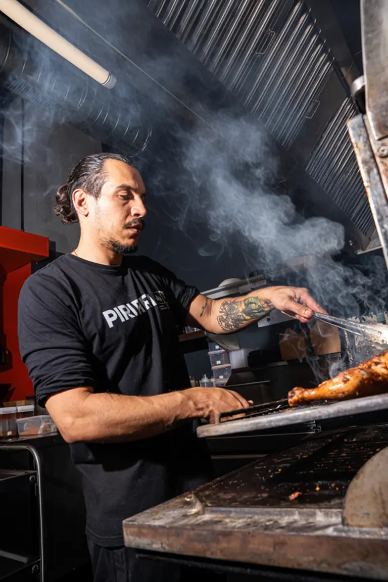 Cocinero de Piri Piri girando el pollo en el horno de carbón